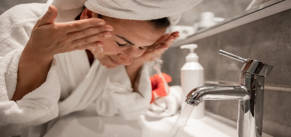 mujer con bata y turbante lavándose la cara en su baño