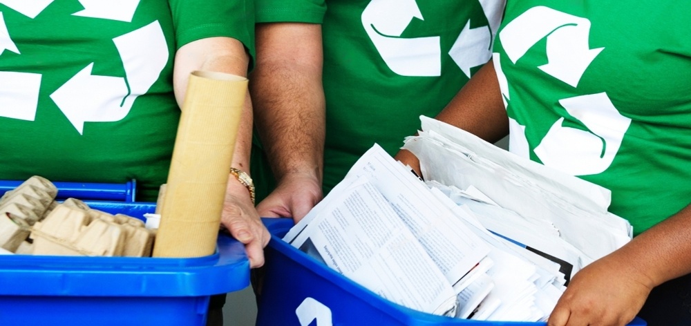 personas con polos con símbolo de reciclaje agarrando baldes con papeles para reciclar